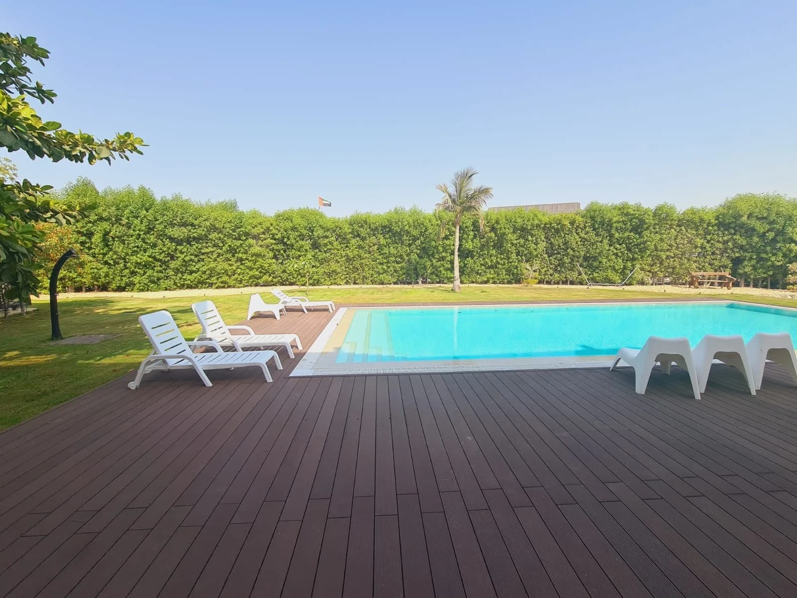 Large outdoor swimming pool with broad timber decking and landscaped grounds